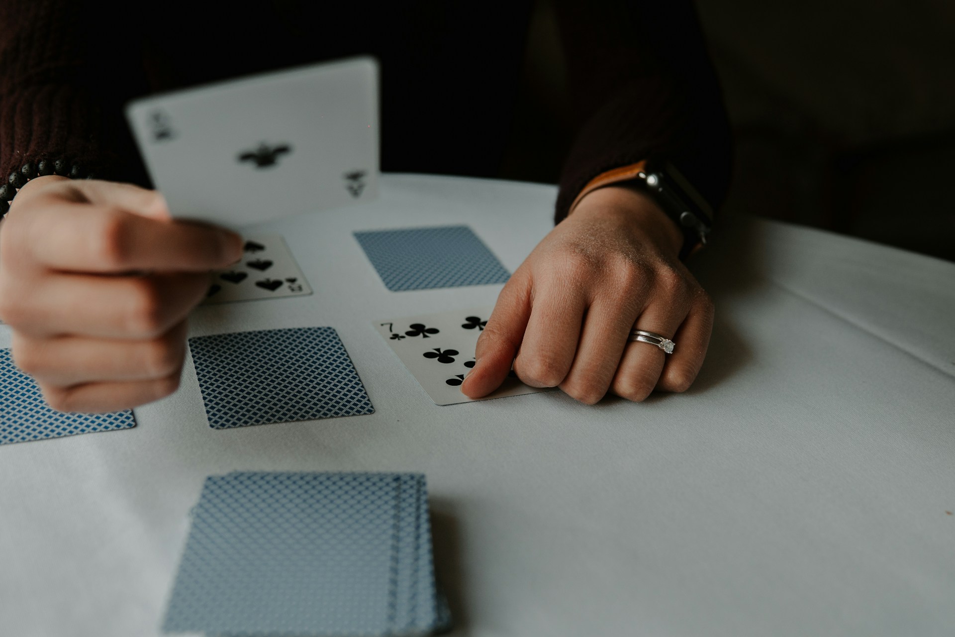 Person holding playing cards on a white table, by Andrik Langfield on Unsplash
