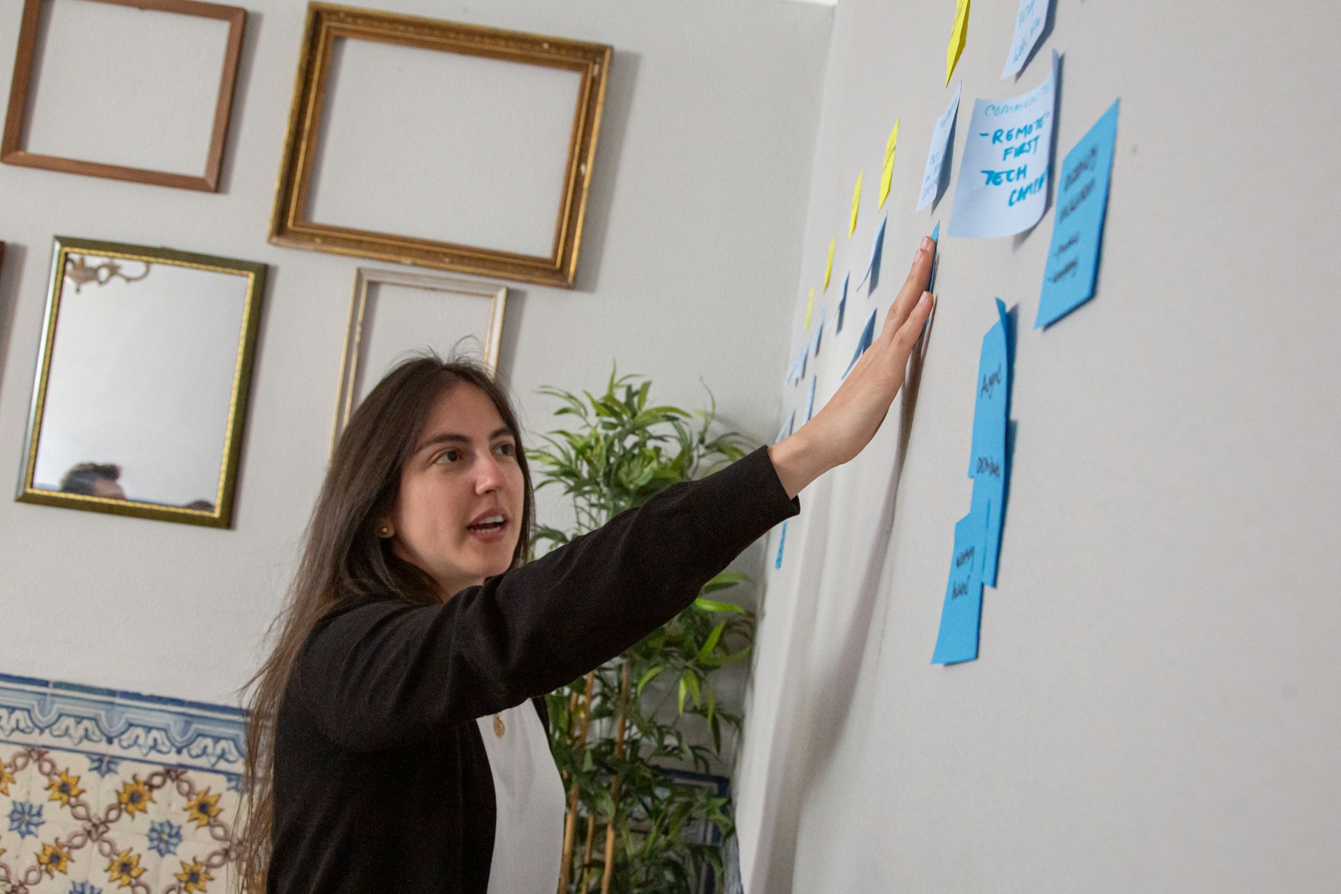 Facilitator pointing at blue and yellow sticky notes on a wall during a team workshop