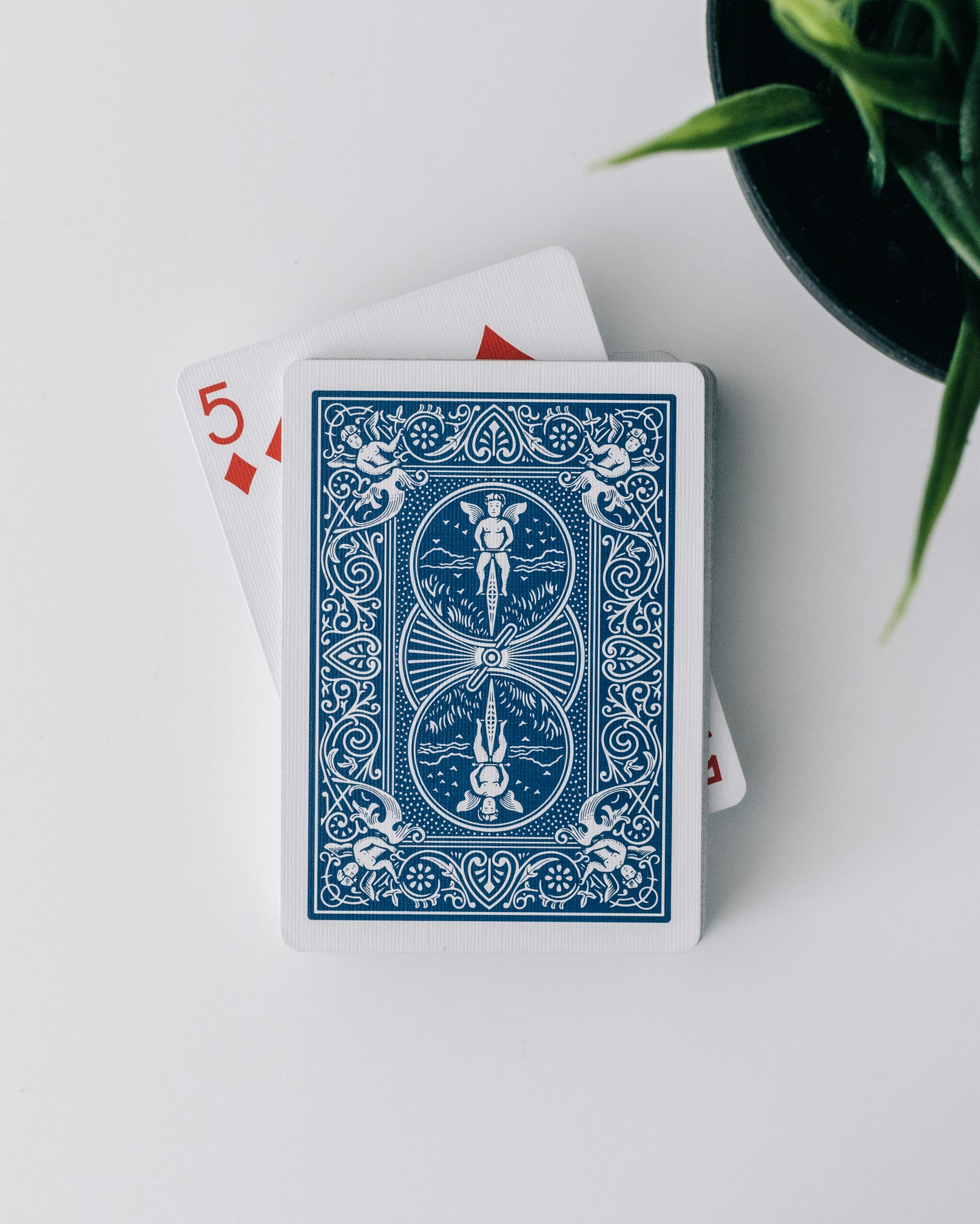 Paquet de cartes à jouer face cachée au dos bleu, un cinq de carreau visible dessous : le seul chiffre apparent qui ancre les autres, par Aditya Chinchure sur Unsplash