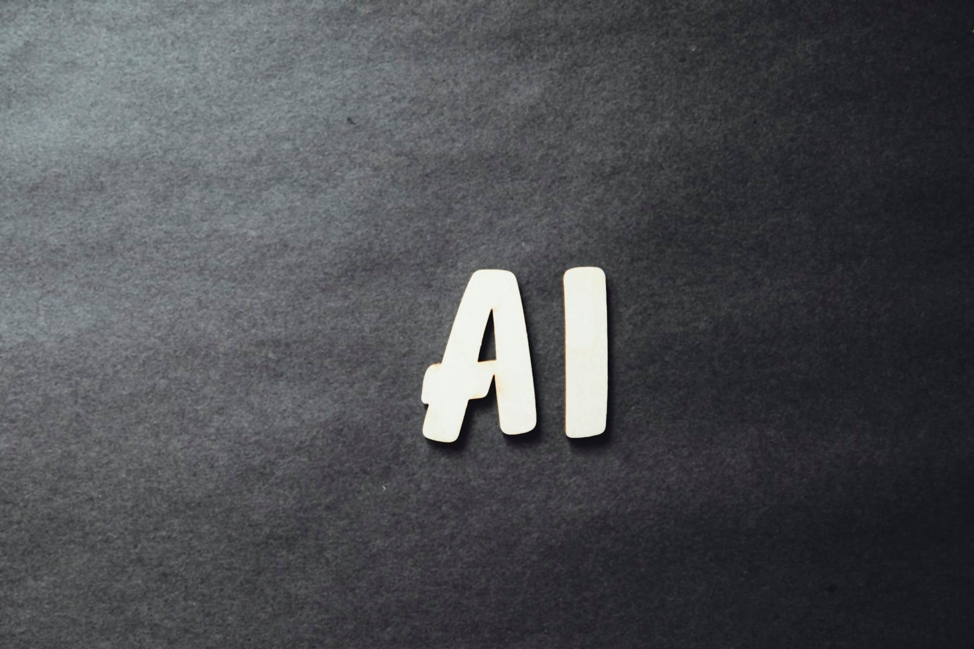 The letters AI cut out of light wood on a dark grey background, the agent that now writes part of the code, by Markus Spiske on Unsplash